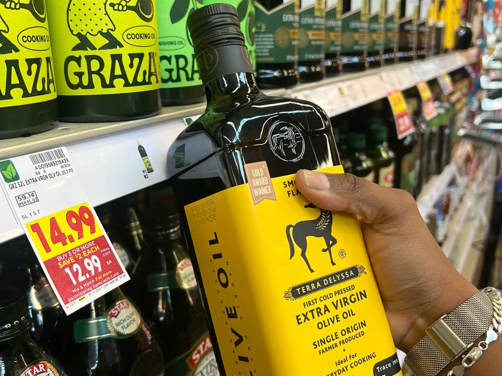 A young woman picks up a bottle of olive oil while grocery shopping at Kroger.