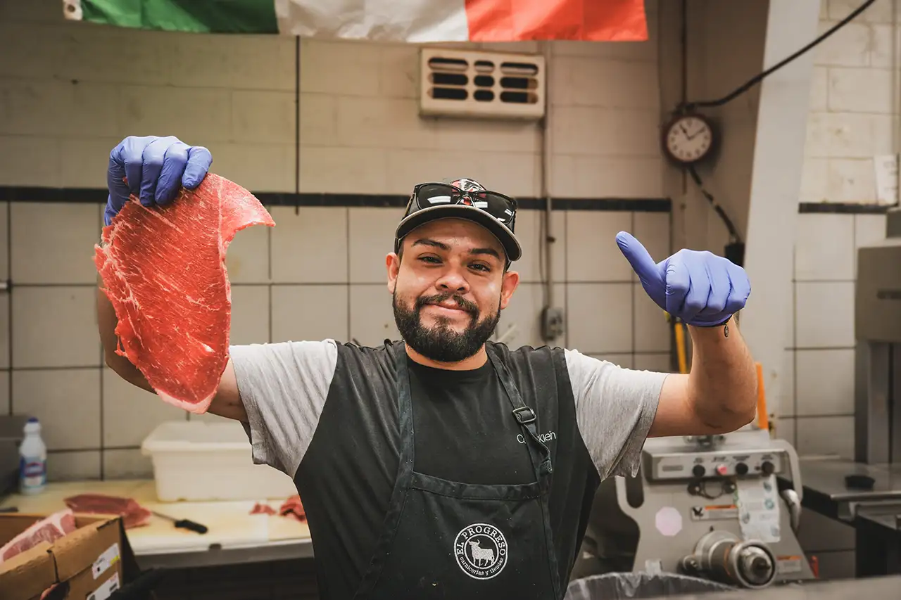 A butcher holds up a cut of meat and a thumb's up inside a meat market in Tri-Cities, Georgia.