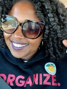 A woman wearing an "I Voted" sticker poses for a selfie.