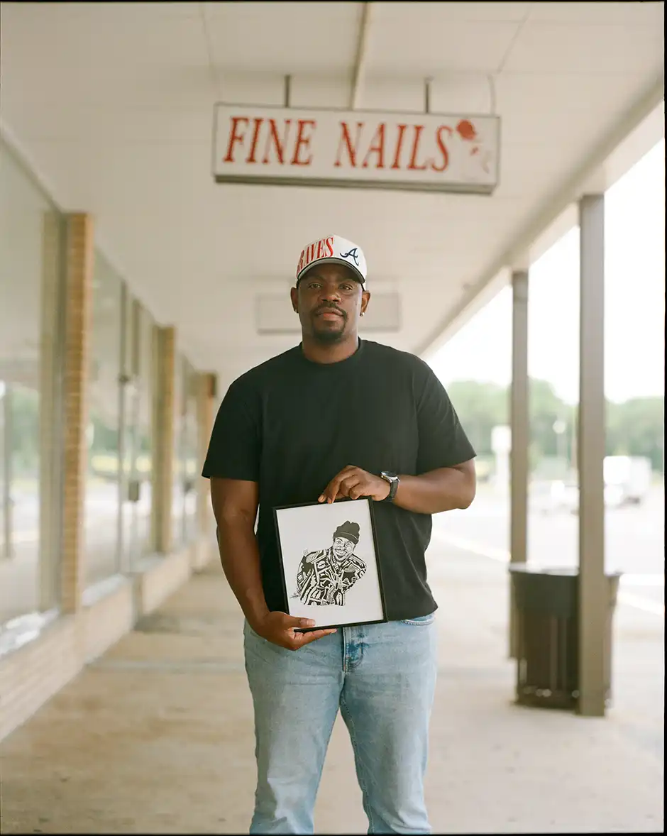 Cedric Smith holds some artwork under a store sign that reads, "Fine Nails".