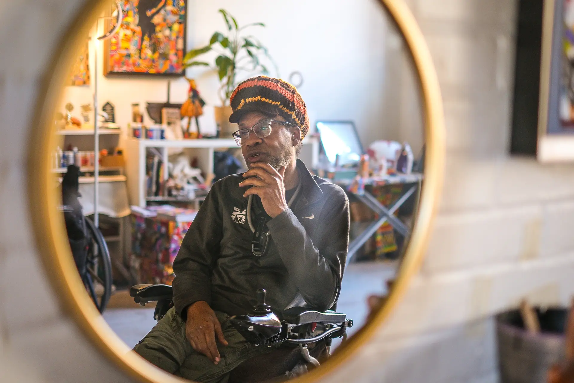 Kenneth Zakee seen through the reflection in a mirror hanging on a wall.