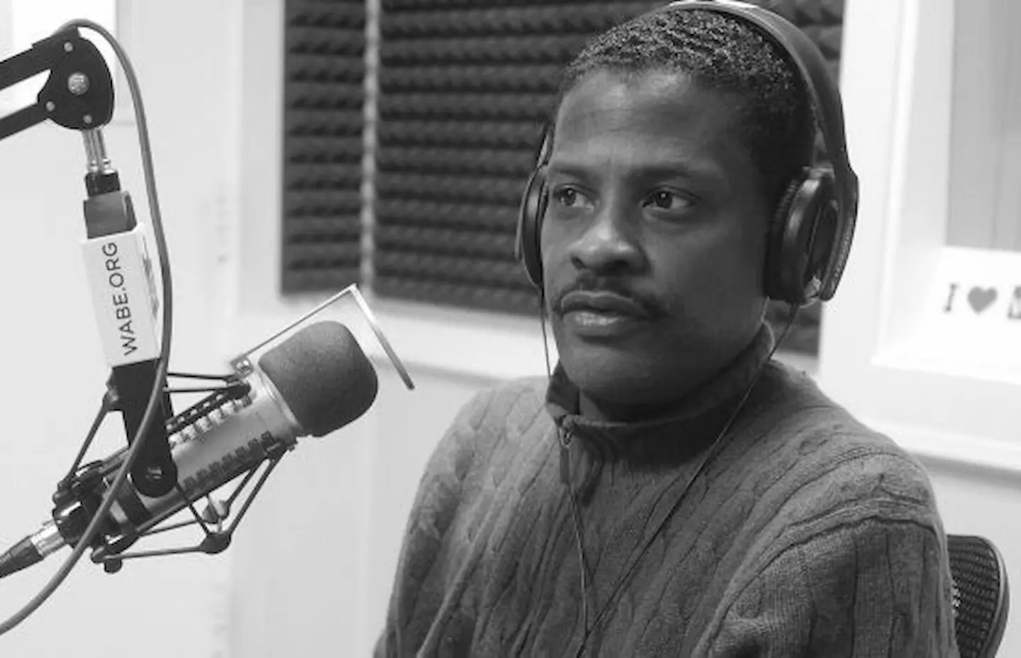 A black man sits in from of a microphone.