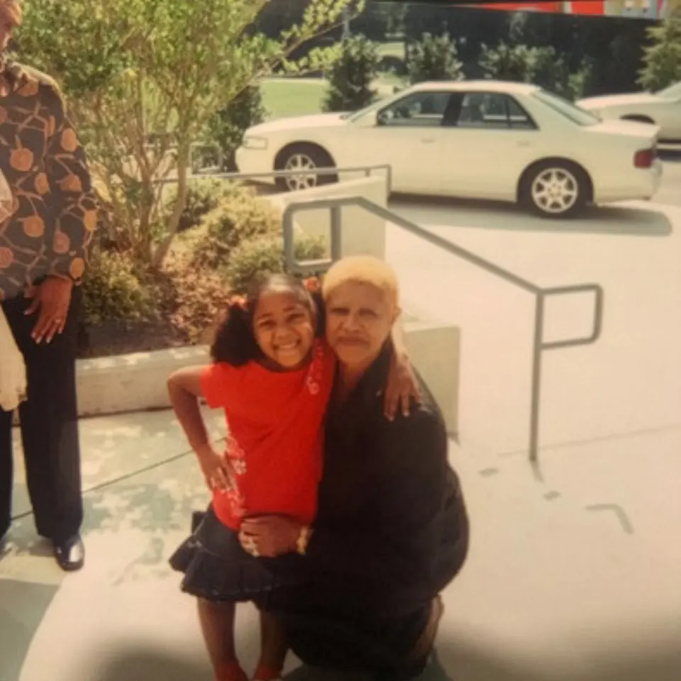 A granddaughter and grandmother hug each other on the steps of a building.
