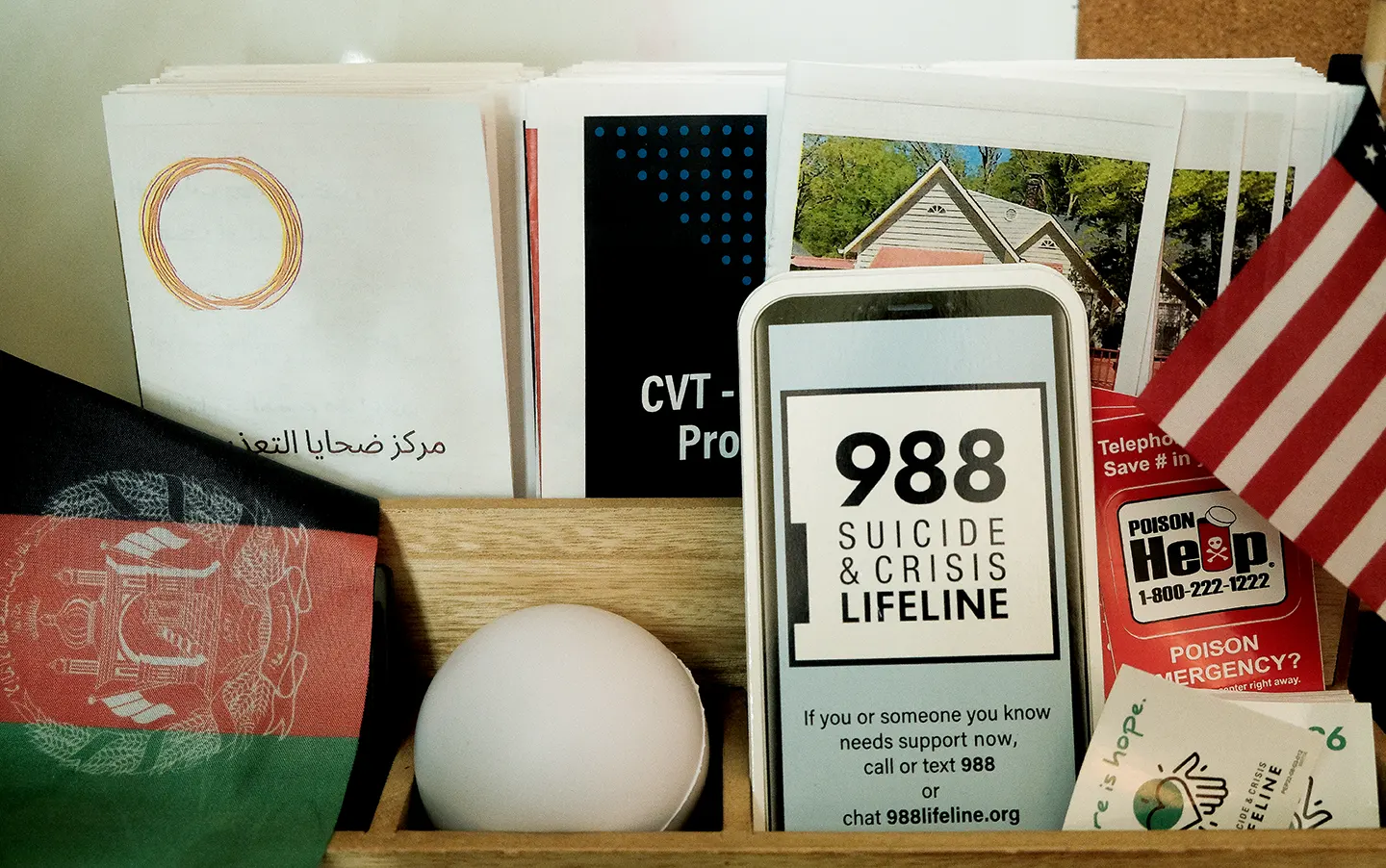 suicide-hotline-cards A brochure holder features literature for the Centers of Victim and Torture, 988 Suicide and Crisis Lifeline, and Poison Help, plus mini Afghan and American flags.